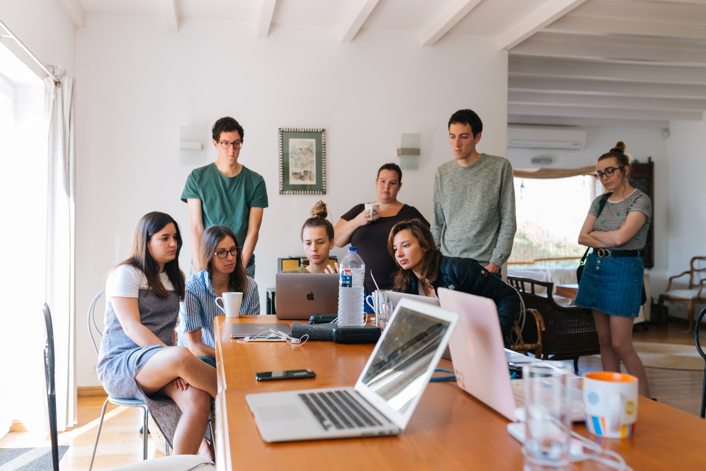 A group of young people gathered around table, watching a laptop