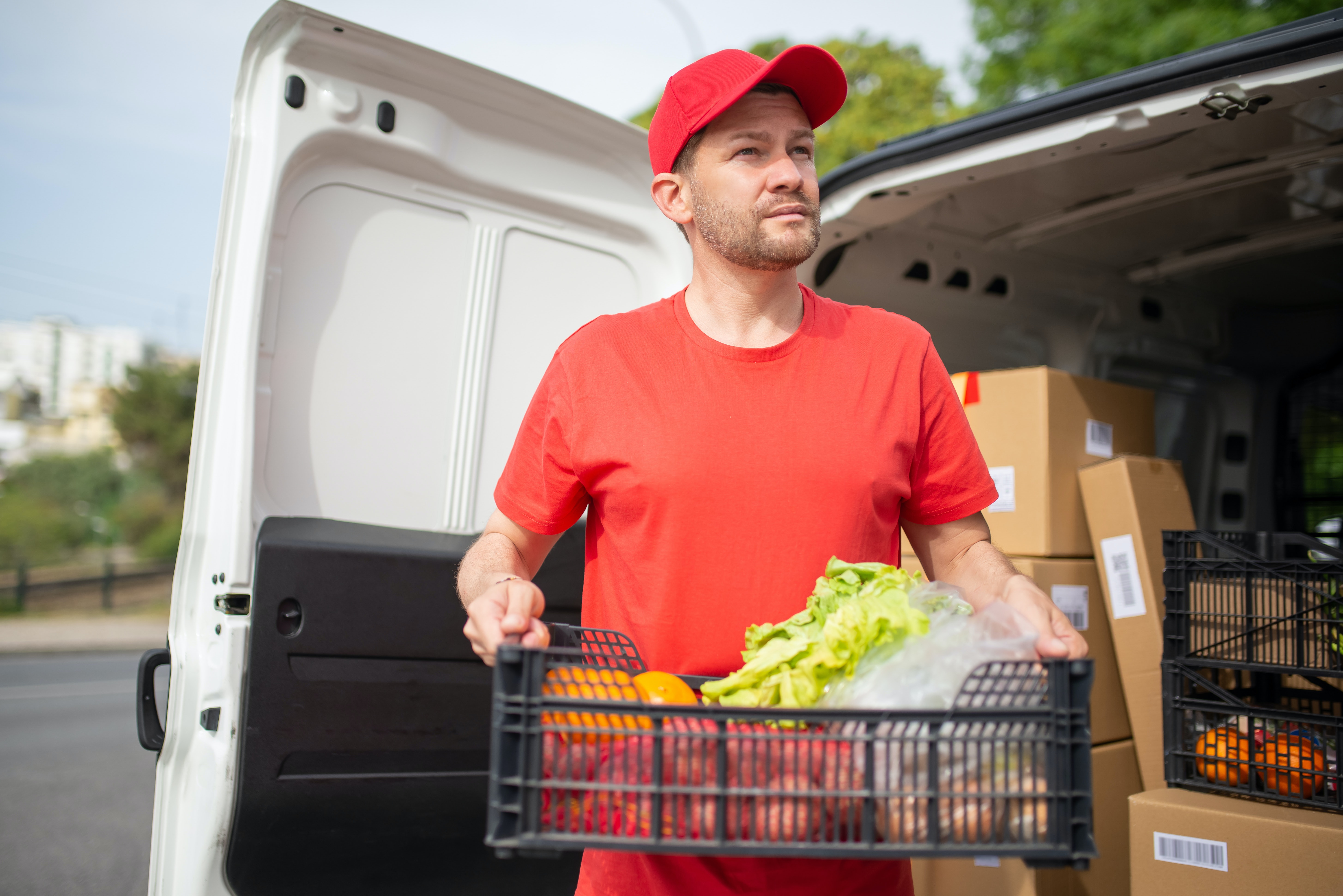 A man in a red t-shirt and hat carrying a box of groceries