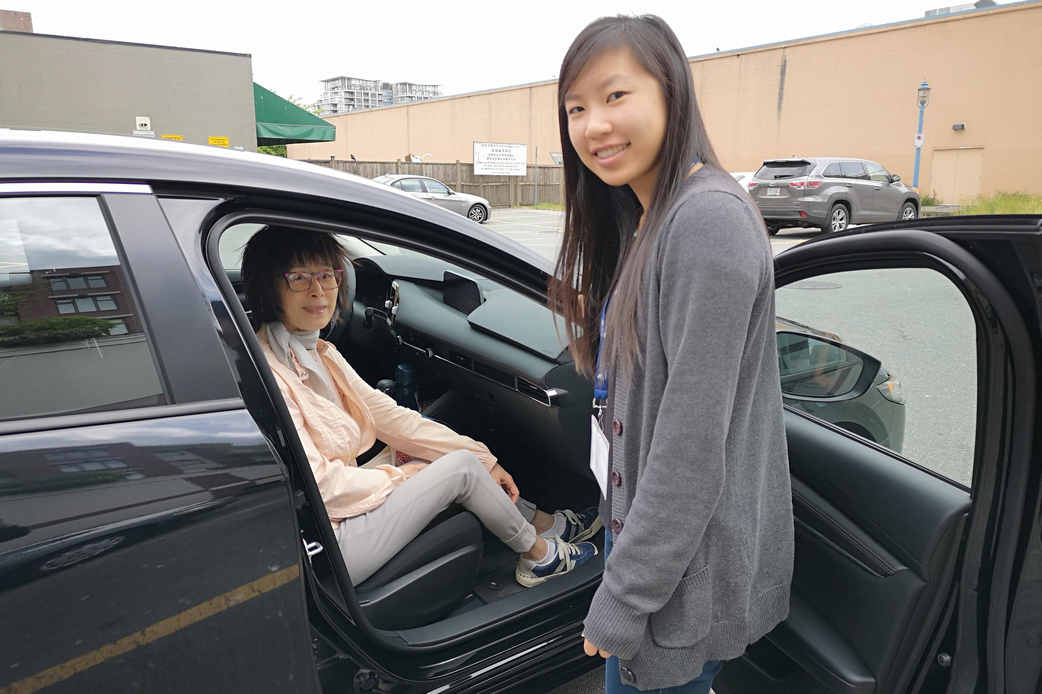 A Woman Sitting in a Car with the Door Open, While Another Woman Stands Next to Her