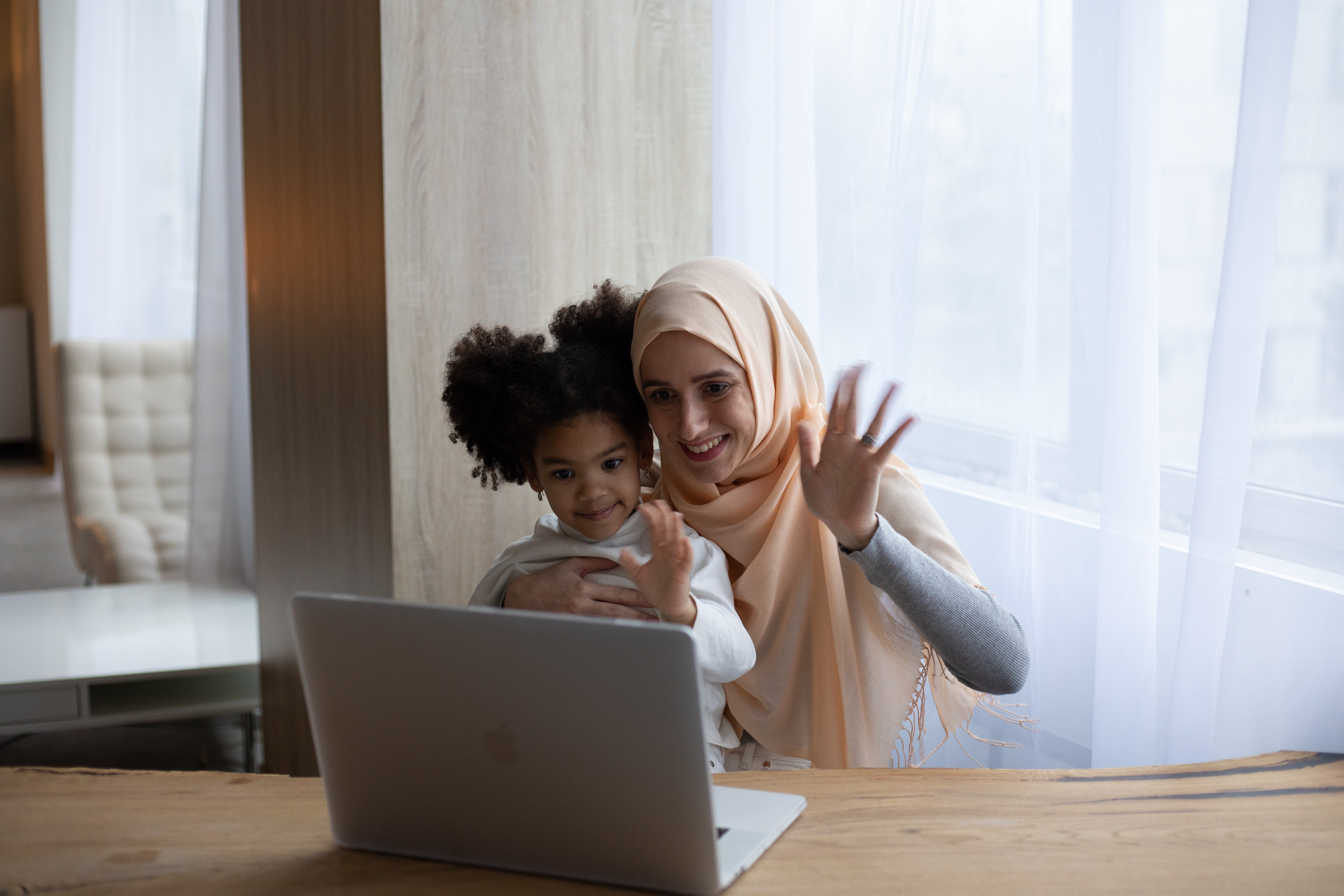 A mother and her young daughter waving at a laptop