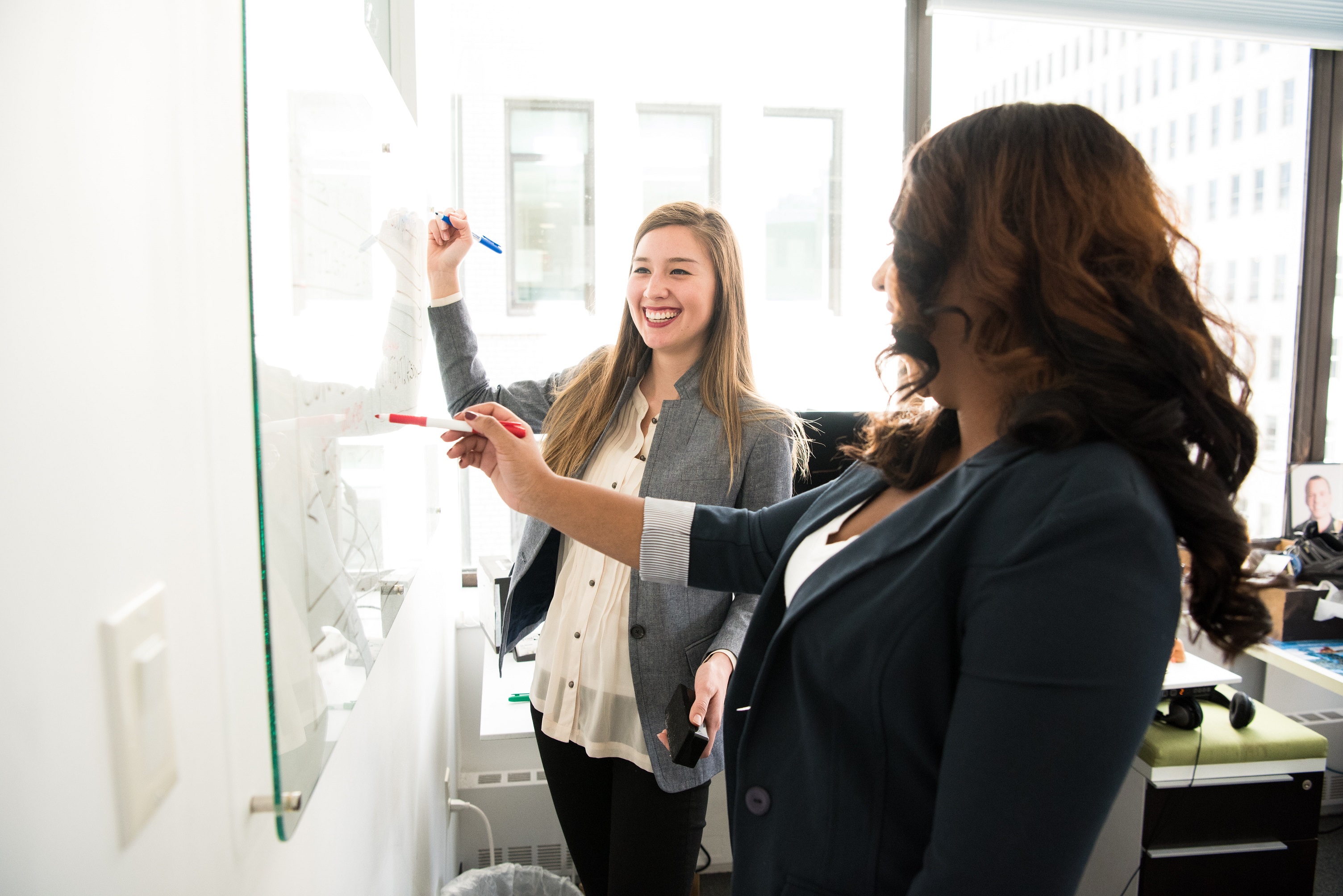 Two women smiling while writing on a whiteboard